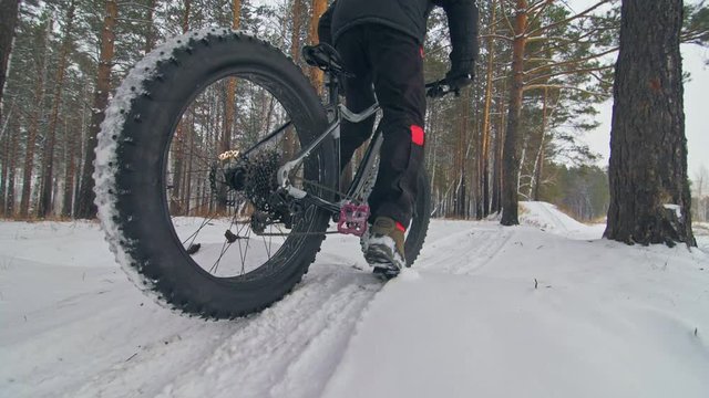 Professional extreme sportsman biker riding a fat bike in outdoors. Cyclist ride in winter snow forest. Man does trick on mountain bicycle with big tire in helmet and glasses. Slow motion in 180fps.
