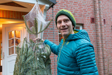 Ein Mann steht mit einen Christbaum vor der Haustür
