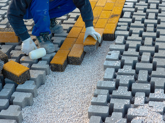 Paving stone worker is putting down pavers during a construction of a city street onto sheet nonwoven bedding sand and fitting them into place.