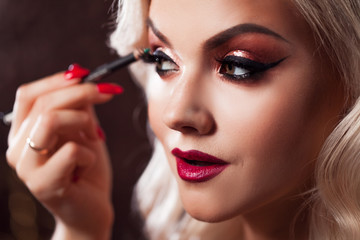 Beautiful young blonde makes a bright holiday makeup. Glamorous make-up. attractive young woman paints the eyelashes