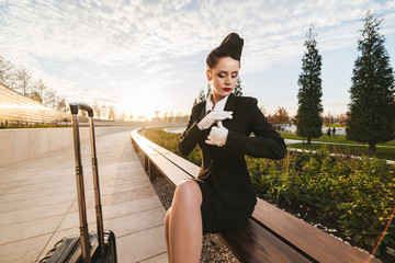 beautiful young woman in uniform waiting for a flight in the park, with a suitcase