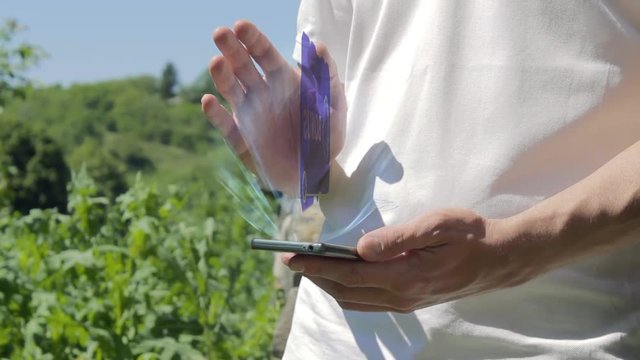 Man shows concept hologram Bonus on his phone. Person in white t-shirt with future technology holographic screen and green nature background