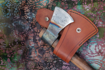 A leather sheath and hand forged tomahawk with color.