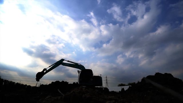 silhouette of digger with sun in construction site