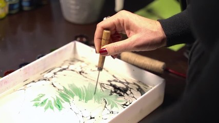 Islamic art - ebru technique, painting on liquid water surface. Paper marbling. Woman drawing with brush, green and black paints. Close up hand. Hobby, arts, culture concept