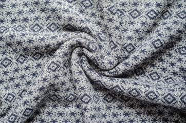 Crumpled background of gray winter sweaters with repeating geometric patterns and small snowflakes. Twisted in the center knitted fabric swatch
