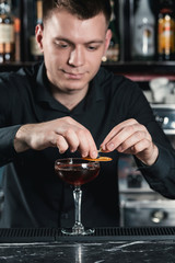bartender making Boulevardier Cocktail Finishing cocktail putting orange slice on top. Bar on a background