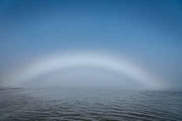 Rare Fogbow or White Rainbow Caused by Dense Fog and Sunlight Over the River