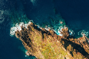 Aerial tropical island view in the middle of the ocean with rocky cliffs and green fields