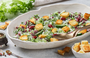 Delicious healthy salad of kidney beans, lettuce, cucumber with bread croutons and yogurt sauce in a white plate. Light gourmet dinner