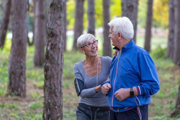 Older couple jogging in the park with distance tracker watch on hands and smile