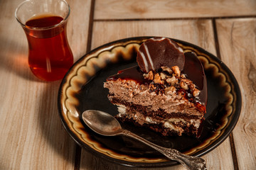 Chocolate cake on a black plate with tea on a wooden background.