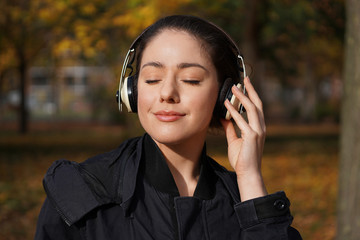 young woman in her 20s listening to music with wireless headphones outdoors - candid autumn lifestyle