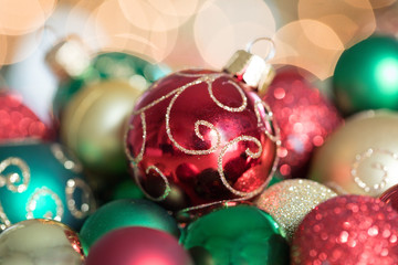 Close up photograph of red, green and gold Christmas ornaments in front of twinkling lights