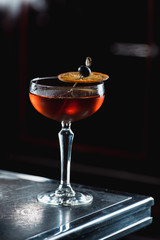 The Boulevardier Cocktail with orange chips on top. On a bar desk