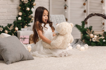 child girl playing with teddy bear near the Christmas tree