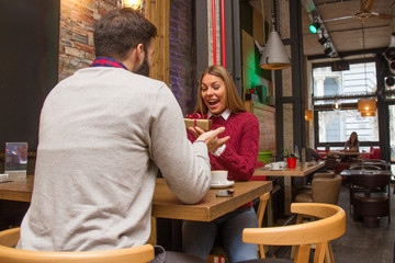 Man giving a present to his girlfriend in cafe and she is surprise