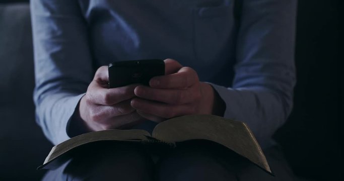 Closeup shot of a woman studying the Bible at home and taking notes on a smartphone.