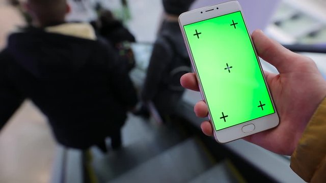 Male hand using smartphone with green screen chroma key in escalator of shopping mall