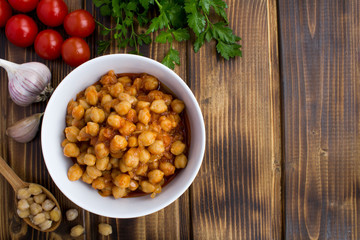 Chickpeas in the tomato sauce in the white bowl  on the wooden  background.Top view.Copy space.