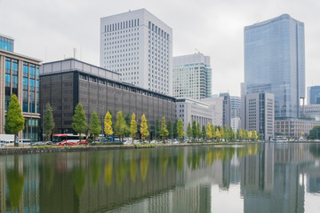 Fototapeta na wymiar Urban background with Tokyo downtown Marunouchi district and water reflections of trees and buildings in November.