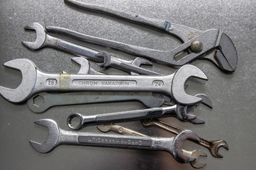 Metal flat wrenches lying on a black shiny table, flat view from above.