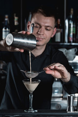 bartender making Espresso Martini cocktail, pouring fluid into glass. Bar on a background