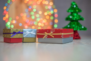 Christmas gifts or present boxes. Colorful lights, Christmas tree in the background, on rustic wooden surface.
