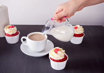 Woman pouring milk on cup of coffee. Three cupcakes with delicious cream with hearts