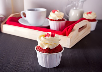 Cup of coffee and cupcakes with hearts on the red napkin on the tray on the wooden table