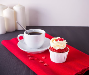Cup of coffee and cupcake with hearts on the red napkin on the wooden table