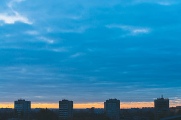 Cityscape with wonderful varicolored vivid dawn. Amazing dramatic blue cloudy sky above dark silhouettes of city buildings. Atmospheric background of orange sunrise in overcast weather. Copy space.