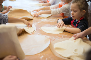 Hands of children rolling pizza dough on the kitchen table. Making pizza. - obrazy, fototapety, plakaty