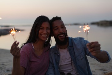 Smiling couple holding sparklers on beach