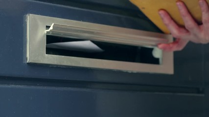 Paper mail being delivered through a door mounted mailbox opening.