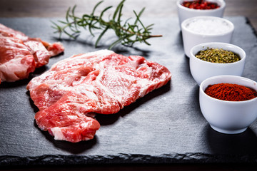 Raw beefsteaks on black stone on wooden background