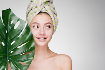 smiling happy girl with a towel on her head arranged a day spa, holding a green leaf