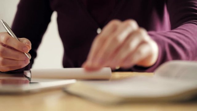 Dolly shot of a young woman taking notes while studying the Bible on a wooden desk or a table.