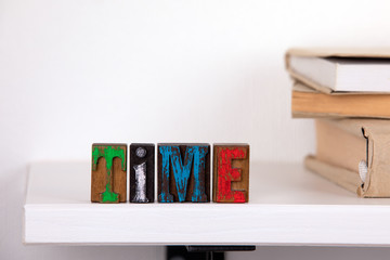 Time word from colored wooden letters un the whitte shelf near books