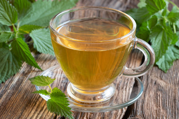 A cup of nettle tea with fresh nettles on a table