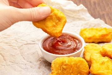 Person dipping chicken nugget in chili sauce indoors