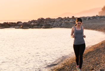 Beautiful young girl run on the beach and smiling. Sunset on the sea at the background. Healthy lifestyle