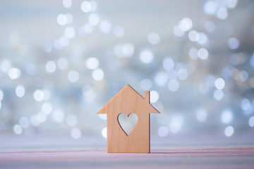 Obraz na płótnie Canvas Wooden icon of house with hole in the form of heart on pastel light bokeh background.