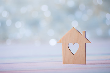 Wooden icon of house with hole in the form of heart on pastel light bokeh background.