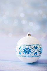 White Christmas ball with blue winter Ukrainian ornament on light bokeh background.