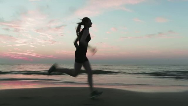 Active sports - young woman runs on a seashore sandy beach by sunset.