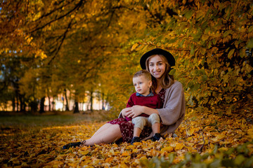 Happy young mother playing with baby in autumn park with yellow maple leaves.Family walking outdoors in autumn. Little boy with her mother playing in the park in autumn