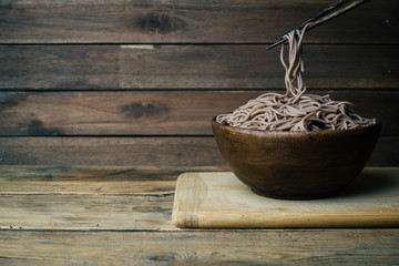 Soba noodles in a wooden bowl on a wooden background. Japanese style. Zen food. Copy space.