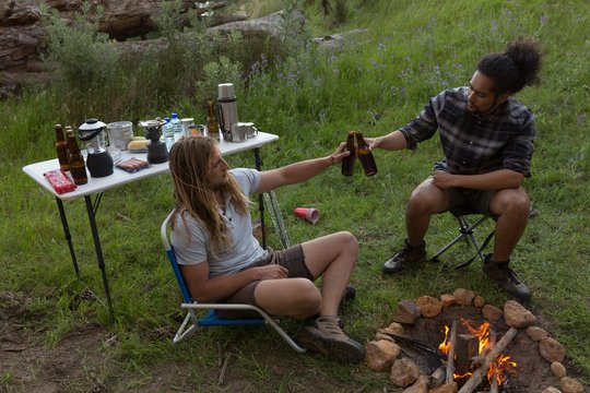 Men toasting beer bottle near campfire