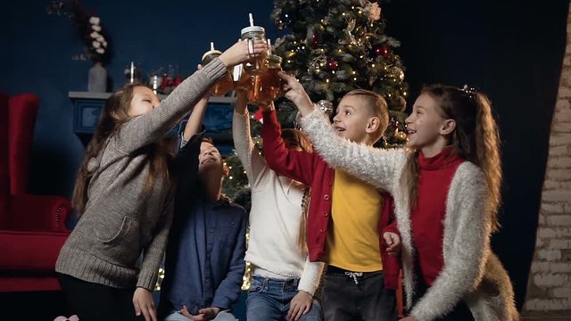 Cute five children cheers cup of tea on the Christmas tree background in cozy room.